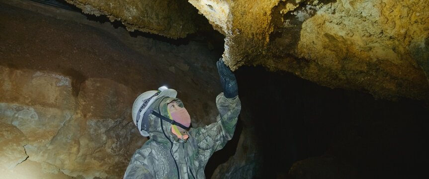 Scientist exploring of cave for geology science. Professional speleology worker in helmet carry out visual inspection on underground nature. Engineer check stalactites.Preservation of earth resources