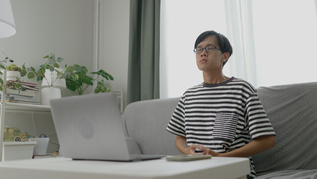  Asian man closes his computer and begins a guided meditation session to relax and clear his mind.