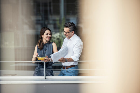 Business professionals discussing over document while standing at office balcony