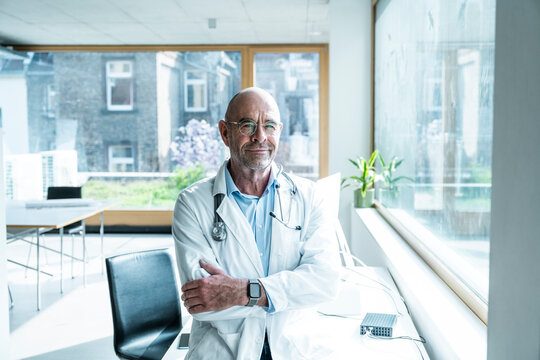 Confident doctor standing in a bright clinic office with arms crossed