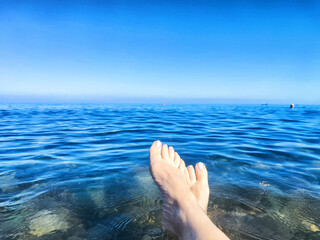 Relaxing feet dangle in clear blue ocean waters under a bright sky