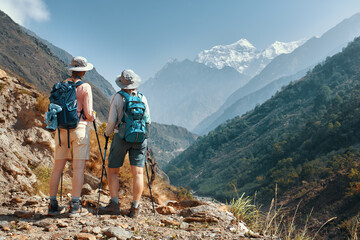 Women tourists with backpacks discuss hiking route against background of beautiful mountain landscape