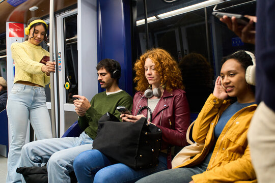 Young people using smartphones and headphones on subway train
