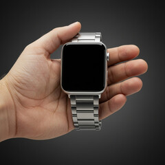 A man's hand holding a silver smartwatch with a blank screen, displaying a modern wearable technology product. Male consumer holding a blank smart watch face against a gray background.