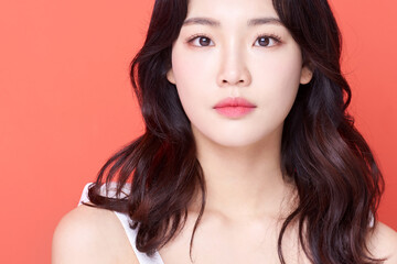 Young Asian Woman with Wavy Hair in White Sleeveless Top on Coral Background