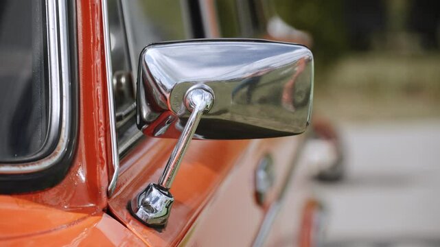 Chrome mirror of old vintage car on sunny day close-up. Retro car exterior from 80s in parking lot and walking people with children in background.
