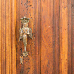 Ornate brass door handle features a figure resembling a celestial being or deity, with folded hands and decorative attire, possibly inspired by Southeast Asian art. The figure has wings.