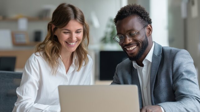 Happy business team of two professionals collaborating in office, working on financial project using laptop, discussing corporate goals and management strategy in modern workspace