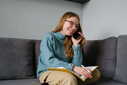 A teenager multitasking by speaking on the phone and making notes in a cozy setting