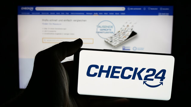 Stuttgart, Germany - 05-25-2025: Person holding mobile phone with logo of German price comparison company Check24 GmbH on screen in front of web page. Focus on phone display.