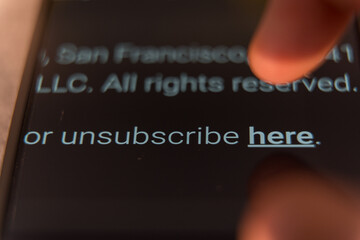 Finger about to tap the unsubscribe here link at the bottom of an email on a smartphone screen