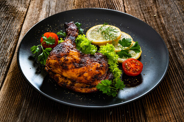 Oven roasted chicken leg with lemon and greens on wooden table	