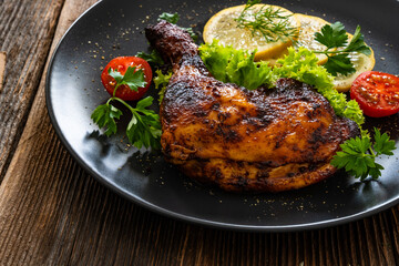Oven roasted chicken leg with lemon and greens on wooden table	