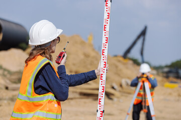 A construction surveyor uses a total station to take measurements while a colleague holds a...