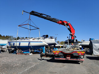A sailboat lifted by a crane in Suomenoja harbor in Espoo, Finland. A man is holding a rope,...
