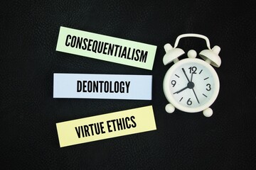 Clock and colored paper with the words consequentialism, deontology, and virtue ethics. The three...
