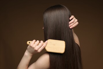 Teenage girl brushing her healthy long hair on brown background