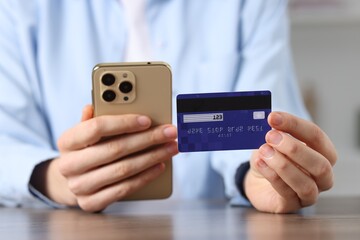 Woman with credit card and smartphone paying online at table, selective focus