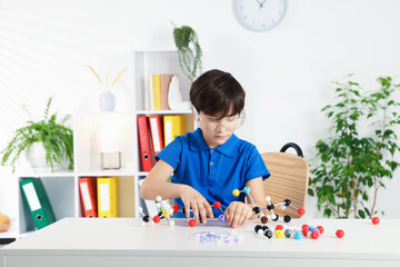 Boy making DNA structure model at desk indoors