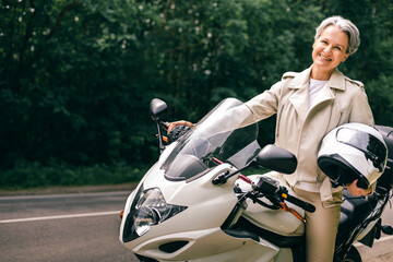 Elegant senior woman with gray hair and motorcycle, smiling freely and embracing active lifestyle