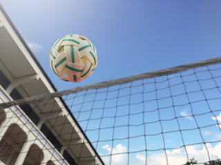 Lookup view image of a yellow plastic sepak takraw ball which floats above the net in the outdoor sepak takraw court, soft and selective focus on ball.