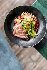 bowl contains a colorful dish with sliced grilled meat, fresh greens, red chili slices, peanuts, and various vegetables. The vibrant presentation and mix of textures make it visually appealing