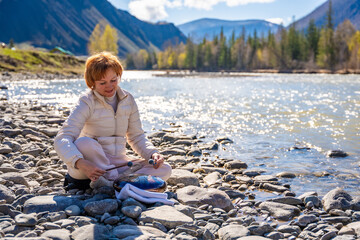 Woman playing a steel tongue drum near a mountain river in Altai, surrounded by wild nature. Concept of spiritual retreat, sound healing, and ancient connection to earth
