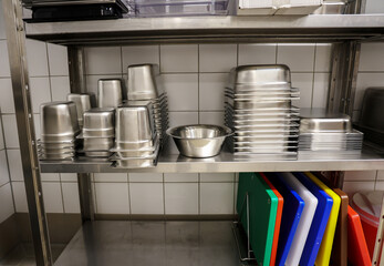 Stacked stainless steel containers and mixing bowls on a clean metal shelf in a commercial kitchen....