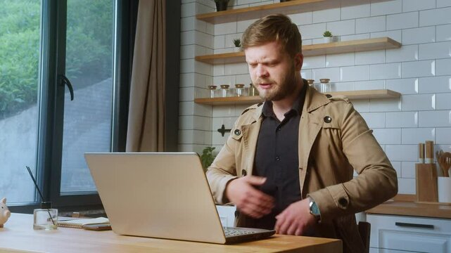Distressed man clutching his chest in discomfort while sitting in front of a laptop, possibly experiencing a panic attack at home.
