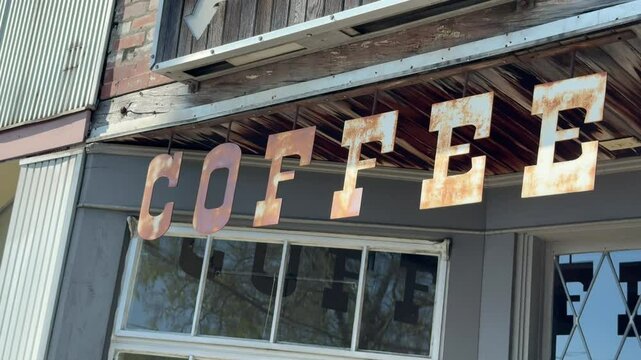 Rustic, rusting coffee cafe sign hanging above the entrance of a ghost town store - isolated street view and panning reveal