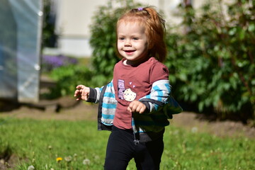 Happy red hair toddler girl running outdoors on a sunny day with arms outstretched, holding a...