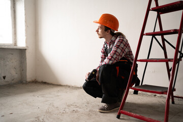 a thoughtful builder sitting at a construction site near a ladder