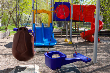 Bright playground featuring toddler and child swings, blue double slide, and red spiral slide...