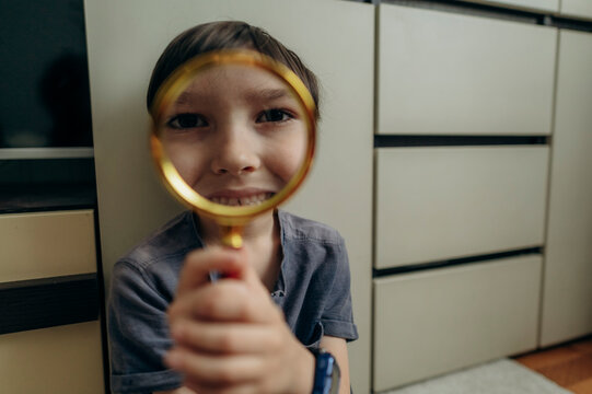 Boy smiling and fooling around with a magnifying glass indoors