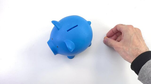 concetto di risparmio, una mano inserisce delle monetine in un salvadanaio in forma di porcellino blu, vista da sopra