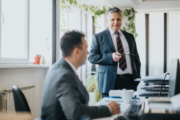 Two businessmen engage in a professional discussion within a bright and modern workspace. Their...