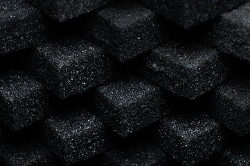 Black Cubes of flexible foam sponges laid out in a pattern. Macro close-up in soft focus. Abstract cubic background