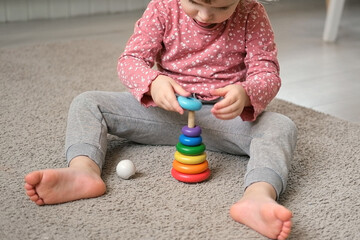 Kid girl play toys at home, kindergarten or nursery. Baby child playing playthings cubes and wood puzzle, pyramid sitting on the floor. Happy preschool education indoor. 3 years old little toddler.