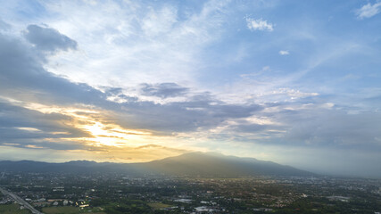 Scenic aerial view of a city sprawling beneath cloudy mountains of Doi Suthep, capturing urban and...
