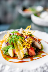 A beautifully plated gourmet dish with fresh vegetables, avocado slices, leafy greens, and decorative edible elements, garnished with sauce and delicate yellow butterfly-shaped crisps