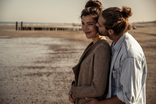 Boyfriend kissing girlfriend on beach during sunny day