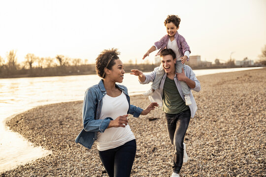Father with son on shoulders running while playing with mother at lakeshore