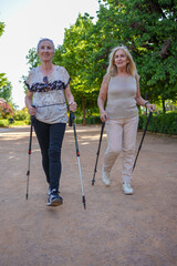 Two senior women practicing nordic walking in a park