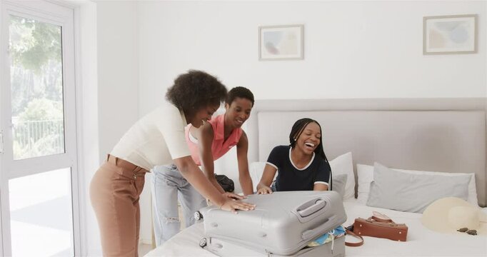 After overpacking suitcase Diverse women friends pressing down filming on phone in bedroom