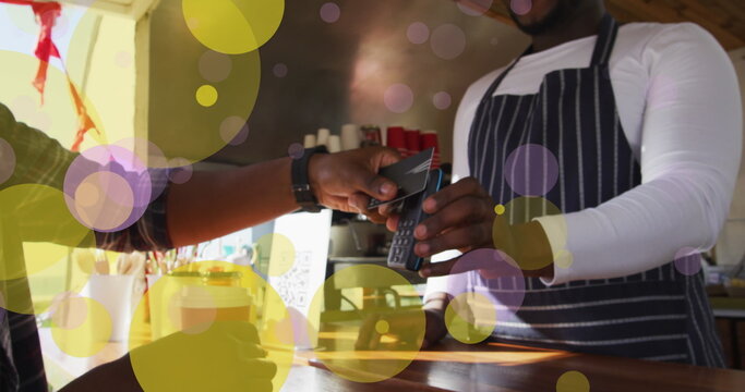 Image of falling yellow dots over people using payment terminal