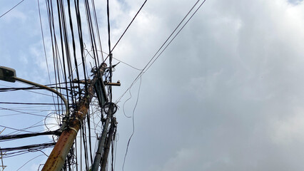 Network of internet provider cables on electric poles, with a cloudy blue sky