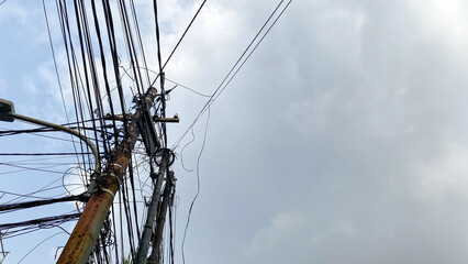 Network of internet provider cables on electric poles, with a cloudy blue sky