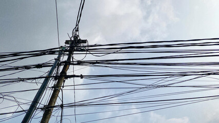 Network of internet provider cables on electric poles, with a cloudy blue sky