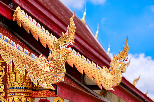 close-up of the ornate golden naga statues adorning the vibrant red roof of a traditional buddhist temple in thailand, set against a bright blue sky. - Powered by Adobe