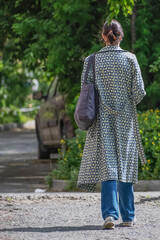 A woman with a shoulder bag walks along the sidewalk on a summer day